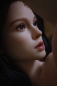 Close-up of a woman's face in profile, showing a brown eye with long lashes, arched eyebrow, smooth skin and pink lips in soft lighting.