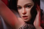 Close-up portrait of a woman with glossy lips and defined makeup, hands framing her face under red lighting.