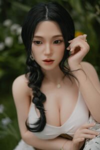 Close-up portrait of a woman with long black hair in a white top, outdoors among greenery, gazing at the camera.