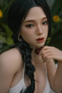 Close-up of a woman with dark braided hair holding a cherry near her lips outdoors.