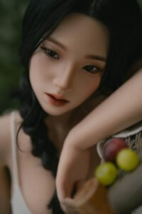 Close-up portrait of a woman with dark hair and soft makeup, resting her chin on her hand with grapes visible at the edge of the frame.