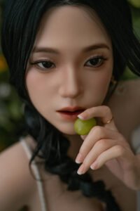 Close-up of a woman with dark hair holding a green grape near her lips, eyes softly looking forward.