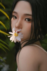 Close-up of a woman with dark hair, a white daisy held near her lips, green foliage in the background.