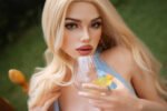 Close-up portrait of a blonde woman gazing at the camera while holding a stemless glass with a lemon slice outdoors.